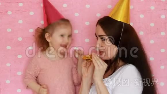 生日快乐。 母女俩戴着节日的帽子吹角，笑嘻嘻的.. 女人和孩子玩得开心