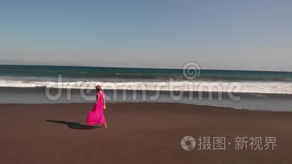 4巴厘岛黑色火山海滩上，年轻女子穿着粉红色连衣裙行走的空中飞行镜头。