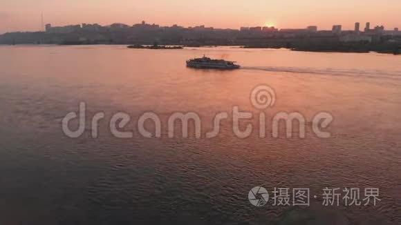 日落时在城市的河流上航行的船的鸟瞰图..