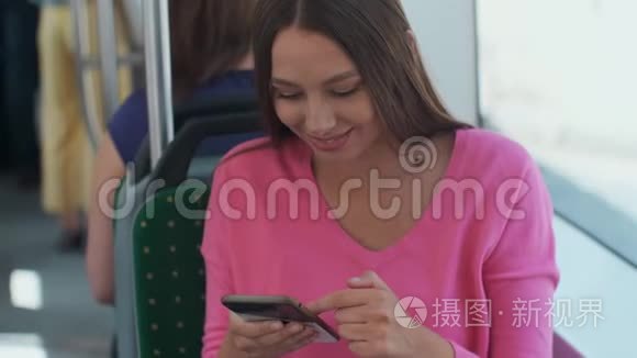 年轻快乐的女人在旅行中坐在靠近窗户的公共交通工具上使用智能手机。