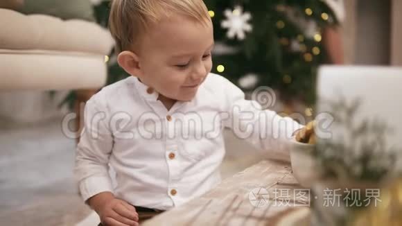 快乐可爱的男孩穿着白色衬衫坐在地板上，背景是一棵圣诞树