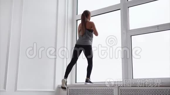 苗条的女人正在大窗户附近做体育锻炼。
