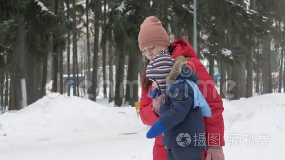 可爱的小男孩和年轻的母亲在冬天和公园里的雪玩耍。 蓝色的孩子`夹克和红色的妈妈。