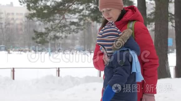 可爱的小男孩和年轻的母亲在冬天和公园里的雪玩耍。 蓝色的孩子`夹克和红色的妈妈。