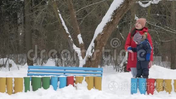可爱的小男孩和年轻的母亲在冬天和公园里的雪玩耍。 蓝色的孩子`夹克和红色的妈妈。