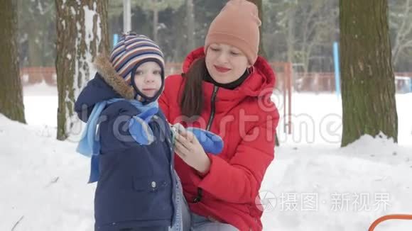 可爱的小男孩和年轻的母亲在冬天和公园里的雪玩耍。 蓝色的孩子夹克和红色的妈妈。