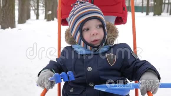 可爱的小男孩和年轻的母亲在冬天和公园里的雪玩耍。 蓝色的孩子`夹克和红色的妈妈。