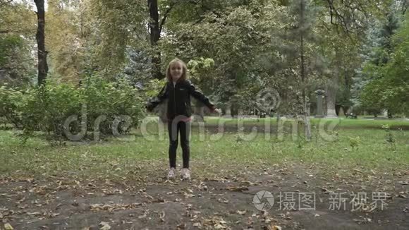 可爱的金发女孩在公园里跳起来，把空气吻送到相机上
