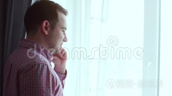 穿格子衬衫的年轻人一边看着窗外一边用红色电话说话