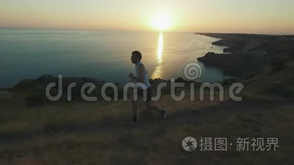运动帅哥正在用手机和耳机做运动，在日落时沿着海岸跑步，然后慢跑