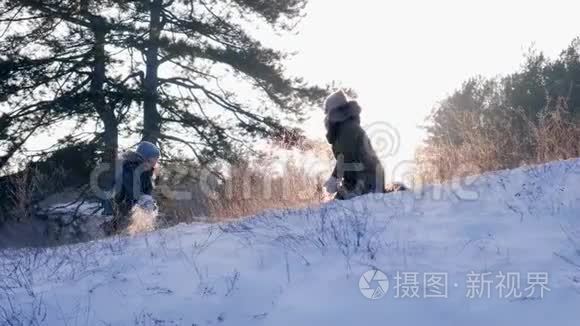 男孩和妈妈在美丽的冬天和户外日落的背景下玩雪