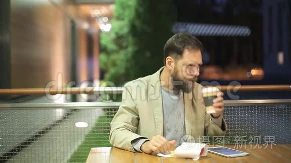 一个长着胡子的白种人中年男子晚上坐在夏季咖啡馆的一张桌子旁观看
