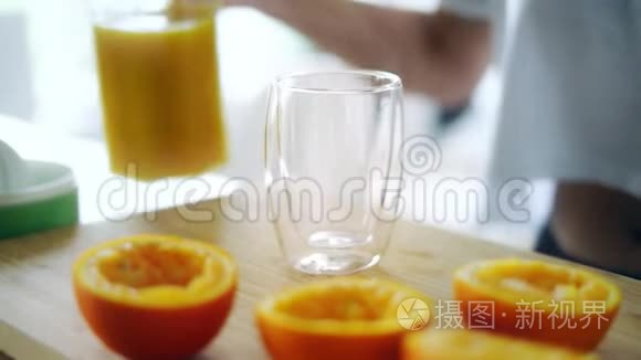 把新鲜橙汁从玻璃瓶倒入玻璃杯中。 挤压橙色部分
