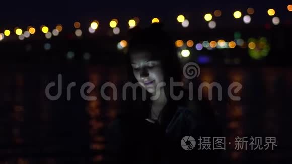 一个女孩很高兴站在一个夜晚城市的背景上使用智能手机