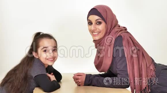 年轻漂亮的妈妈和她的小女儿戴着头巾，看着镜头，笑着说家庭，幸福的家庭观念