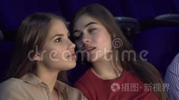 两个快乐的女朋友在看电影时窃窃私语