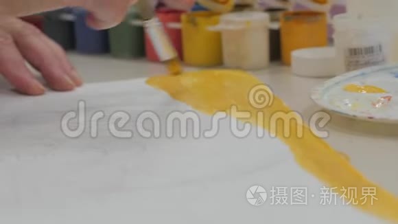 艺术家在画布纸上画一条黄色的画，艺术家在工作室里，造物主做一个刷子的运动。