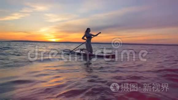 冲浪女人在冲浪板上，在夕阳下漂浮在水面上。