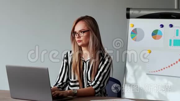 一幅美丽的欧洲女孩坐在办公室的笔记本电脑前的肖像，上面有一件白色衬衫，上面有图表和图片
