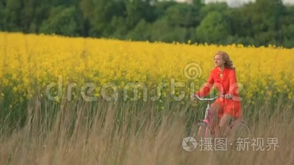 一位穿着红裙子的漂亮金发女郎正快乐地骑着自行车沿着盛开的黄色田野