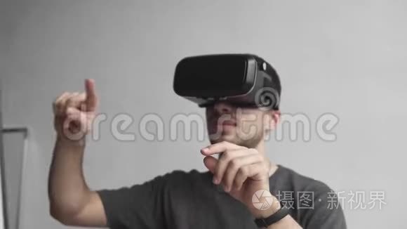 年轻人戴着虚拟现实护目镜，坐在办公室里对着电脑，试图触摸物体