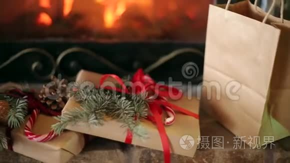 圣诞礼物装饰着云杉树枝，球果，丝带放在壁炉旁.. 温暖的原木着火了。 圣诞节