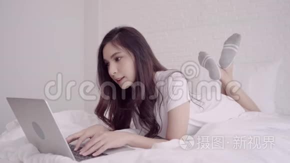 美丽的亚洲混血白人妇女使用电脑或笔记本电脑，而躺在床上在她的卧室。