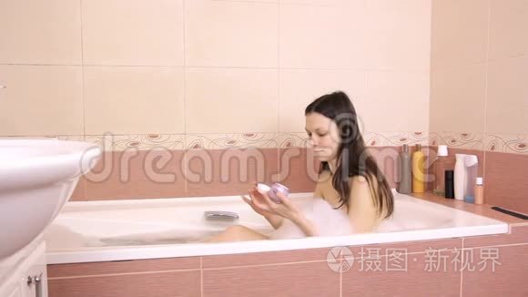 美丽的女人用粘土面具打开一个罐子。 把面具涂在她脸上。 家庭浴室。