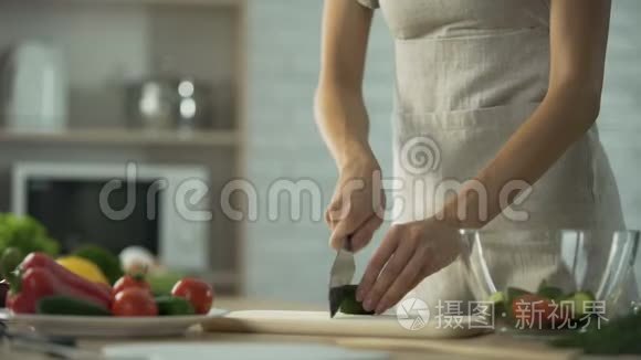 女人一边切黄瓜，一边在家里的厨房做沙拉