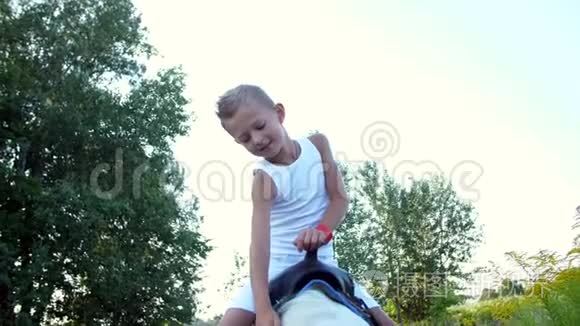 一个七岁的男孩，穿着白色T恤，坐在一匹小马上，抚摸着他.. 开朗，家庭假期愉快.. 户外，在