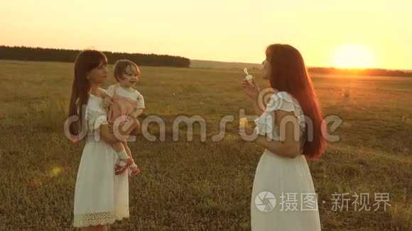 女儿们欢乐而微笑，夕阳下，泡泡在公园里飞舞。 慢动作。 快乐的妈妈在玩孩子吹肥皂