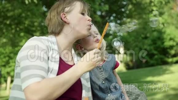 快乐的年轻妈妈和女儿在夏天的公园里吹肥皂泡