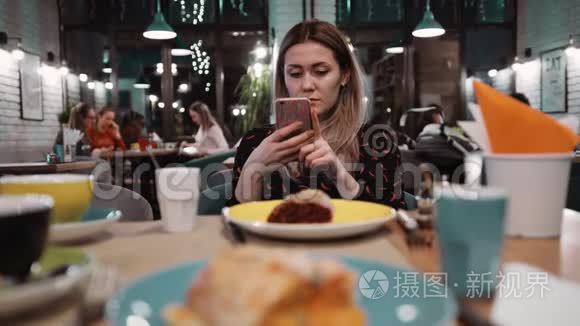 一个年轻女孩在餐馆里用手机。 桌子上有一个餐厅里的甜点，一把叉子和一把刀。