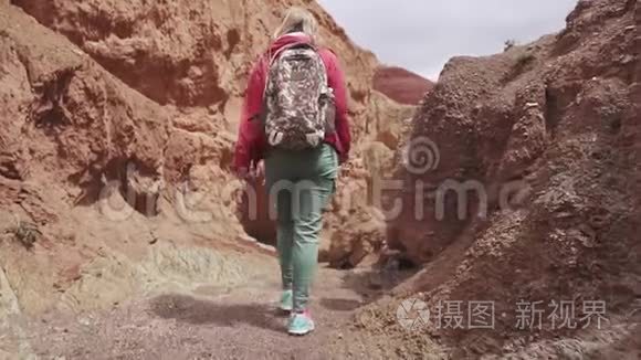 一个带背包的旅行者沿着不寻常的地形行走。 后景。 红色的山脉和红色的地球就像火星一样。