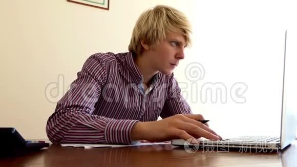 年轻人在办公室里写了一份文件，看着他的计算器和一台电脑
