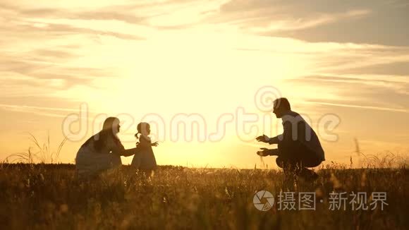 爸爸妈妈和孩子在公园里玩日落，孩子迈出第一步。 幸福的家庭玩他们的女儿