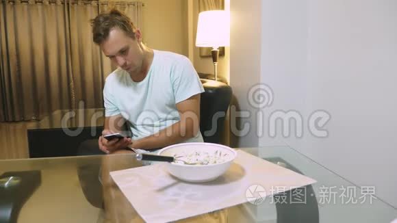 一个疲惫的人坐在客厅的桌子旁，吃晚饭，用电话。