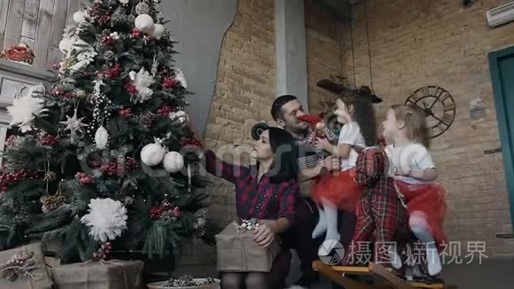 幸福的家庭一起装饰圣诞树。 父母和两个女儿在圣诞礼物上玩耍