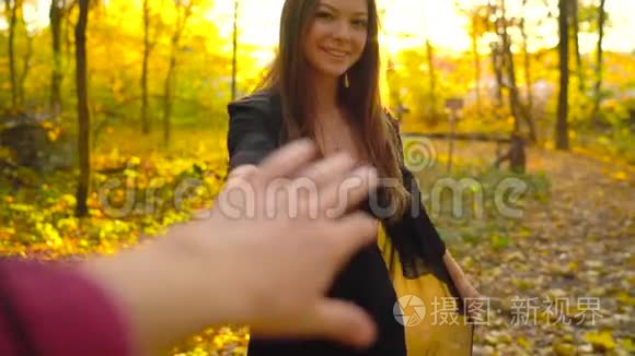 美丽的女孩牵着男朋友的手，跟着他穿过黄色的秋天森林。