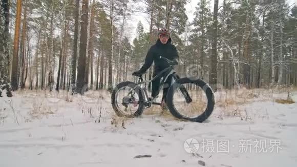 专业的极限运动员自行车站在户外一辆胖自行车。 骑自行车者在冬天的雪林中退缩。 男人走路