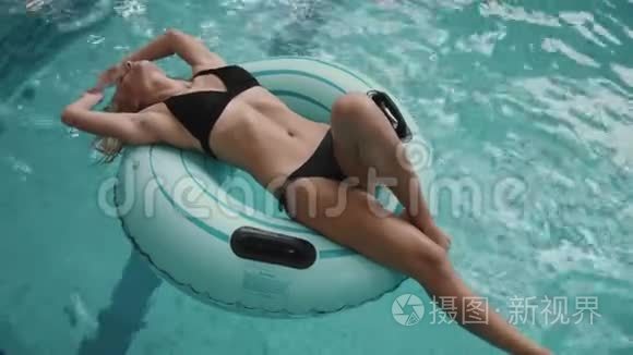 迷人的女人穿着黑色比基尼在游泳池里的充气橡胶圈上游泳。 4k.