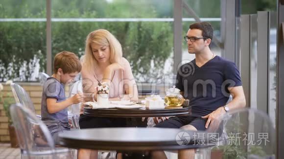 妈妈看着男孩在餐厅的露台上一起吃饭
