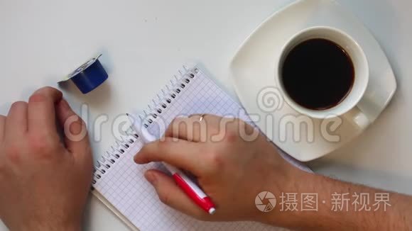 男人在咖啡里吃奶油。 然后他拿起一支笔，思考在笔记本上写什么。 他不时地喝咖啡