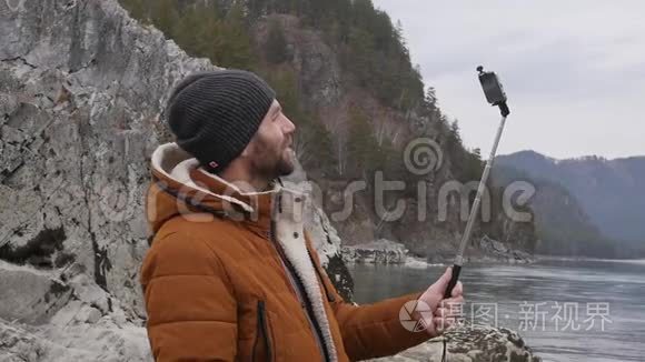 大胡子的游客正在与朋友在一条山河畔的手机上举行视频会议。 慢动作