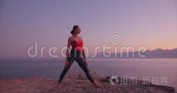 穿红色衣服的白人妇女在日落时在海边的悬崖上练习瑜伽，放松身心。