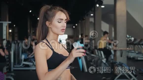 年轻的运动女性在锻炼后在健身房喝水。