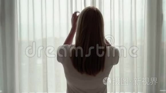 穿白色t恤的女人揭开窗帘，看着窗外。 在外面欣赏海景