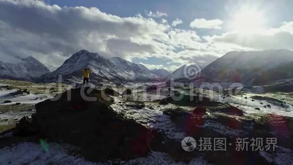 孤独的登山者在云层上方的雪山上休息，进入太阳，登山者到达雪山的顶端
