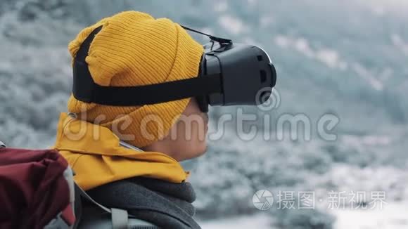 穿着黄色外套享受虚拟现实眼镜耳机或在冬季山区户外玩3D游戏的年轻魅力男子