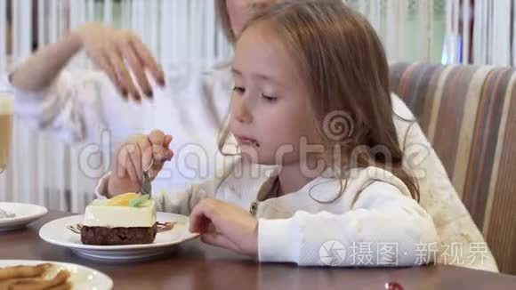 美丽的年轻母亲和小女儿一起在一间舒适的咖啡馆里吃蛋糕